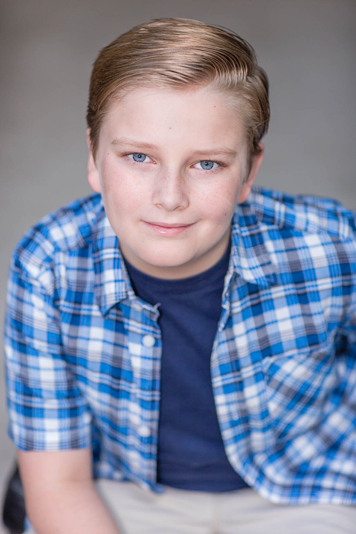 Actor headshot of a boy with blue eyes in blue plaid shirt.
