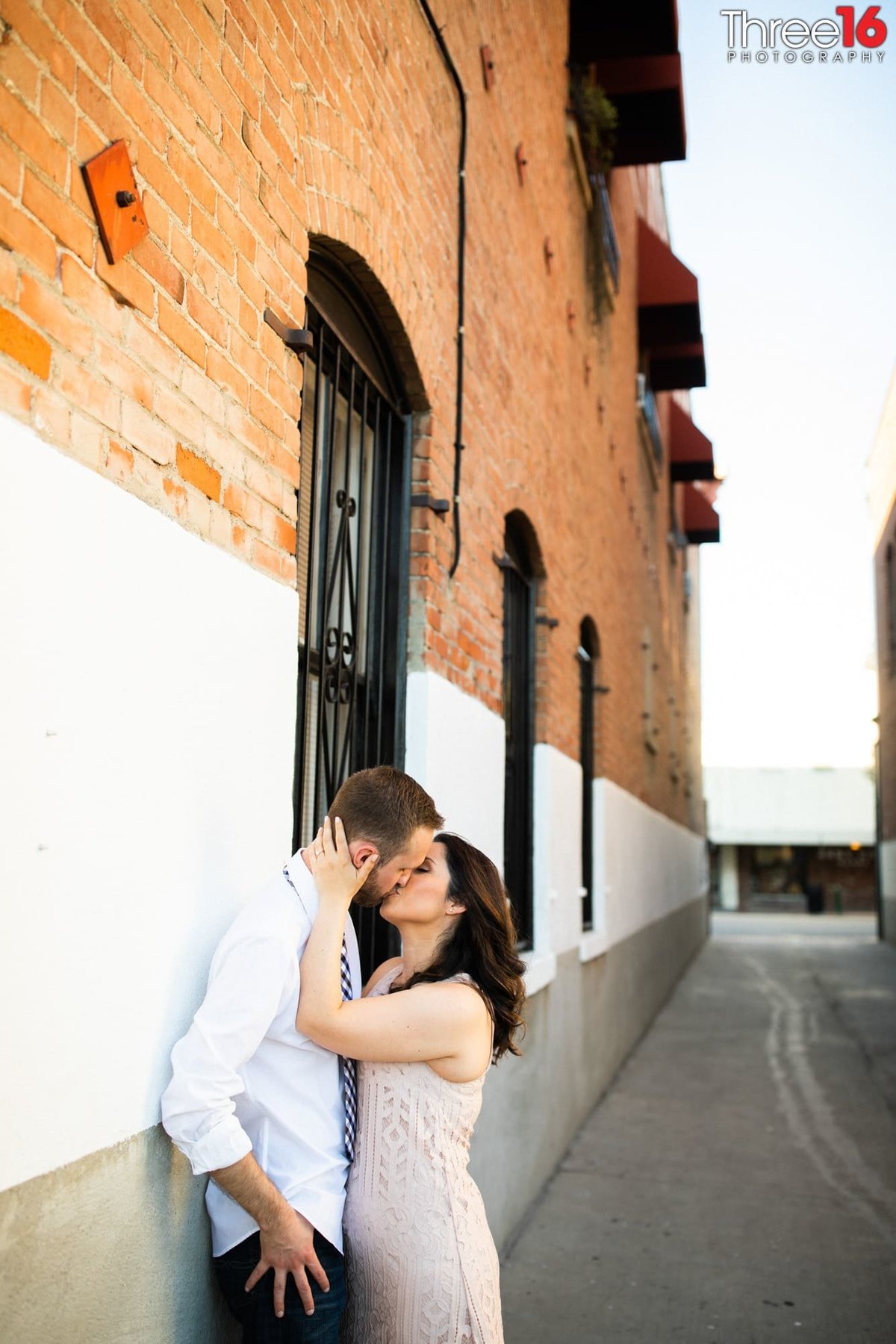 Bride to be kisses her Groom as he is up against a wall in an alleyway