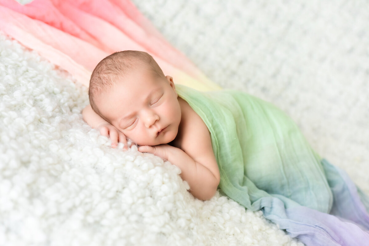 Newborn Photographer, a baby lays on soft blankets and is wrapped in a colorful blanket