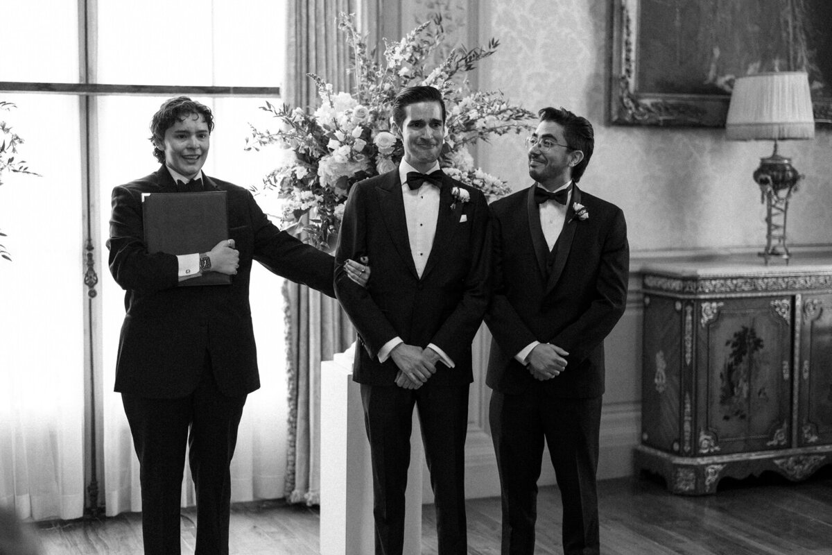 Officiant and best man supporting the Groom while he cries as his Bride walks down the aisle for their wedding ceremony at Rosecliff Mansion in Newport Rhode Island, captured by Andrea-Marie Photography