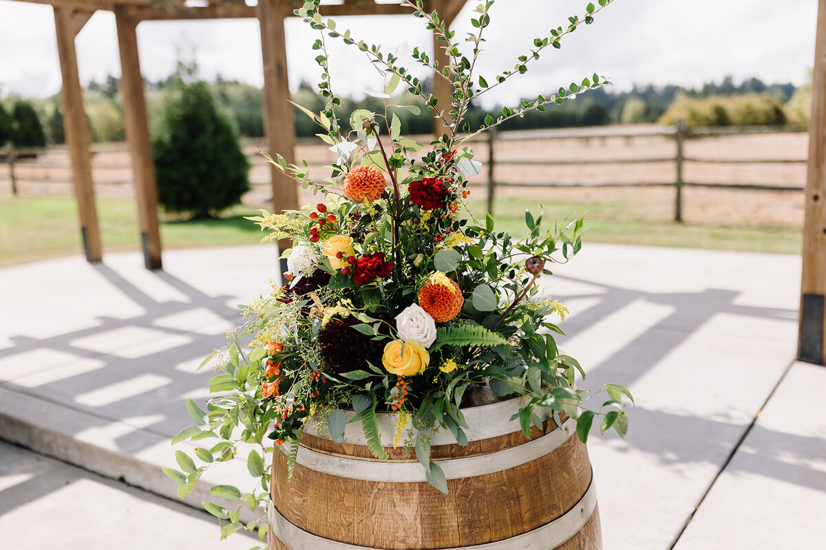Ceremony arrangements made of flowers in orange, red, mustard and burgundy on top of wood wine barrels.