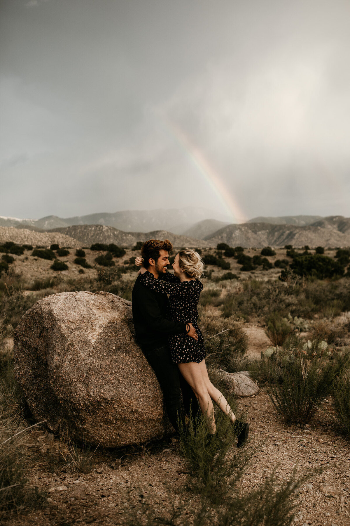 engaged couple hugging in front of a rainbow