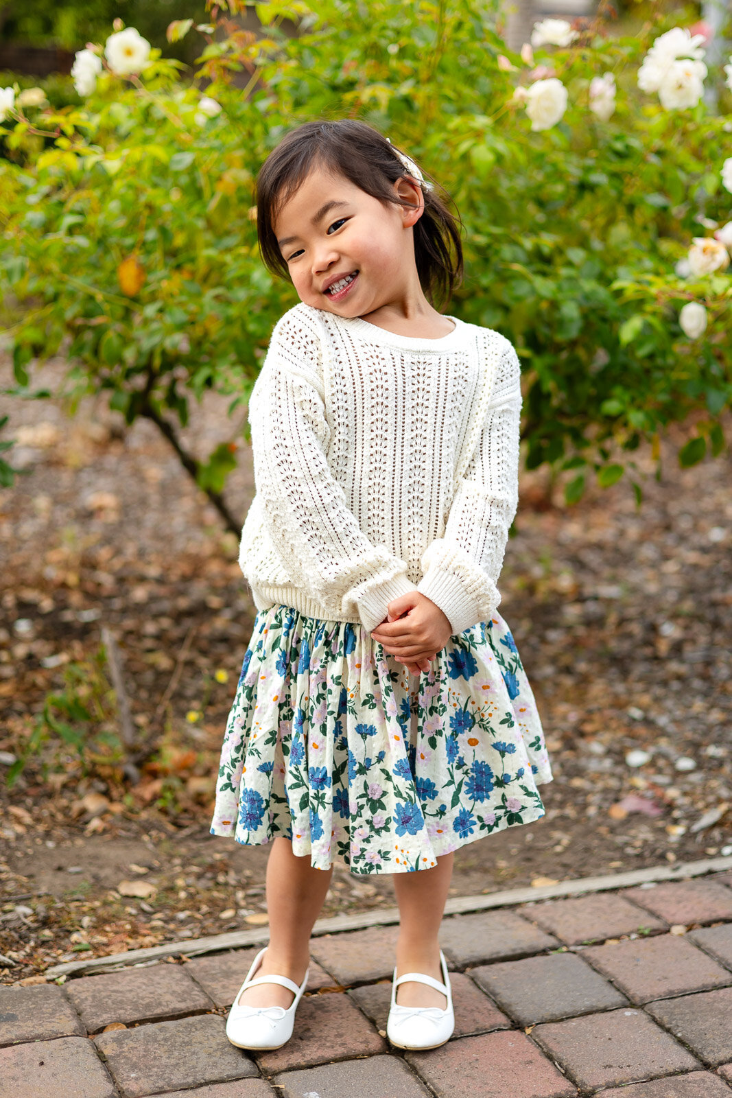 Smiling preschool girl in floral skirt posing in rose garden for Bay Area lifestyle school photography – Ellobelle Photography