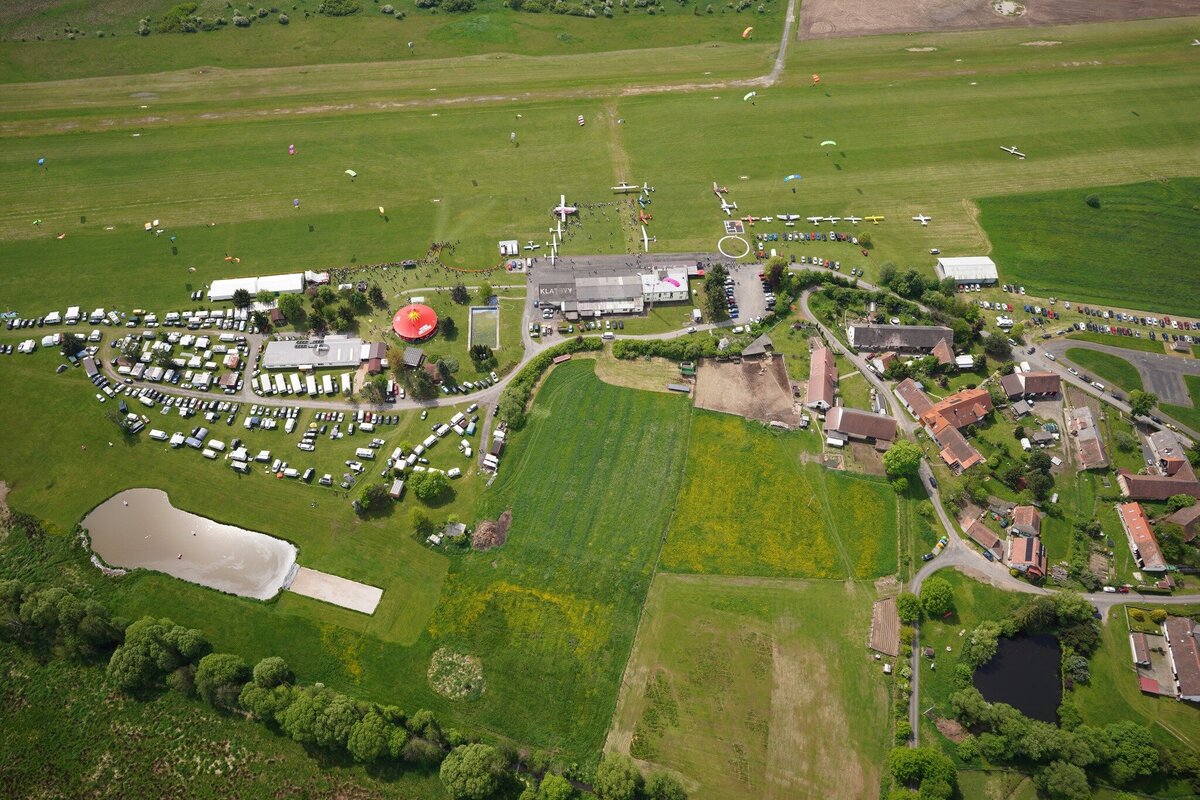 Das Bild zeigt den Sprungplatz in Klatovy von Oben. Es ist die grüne Wiese und der Camping Platz zu sehen während Fallschirmspringer landen