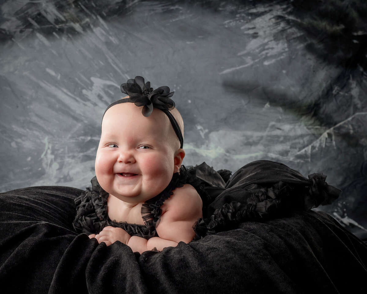 A little girl lays on a black rug and smiles big