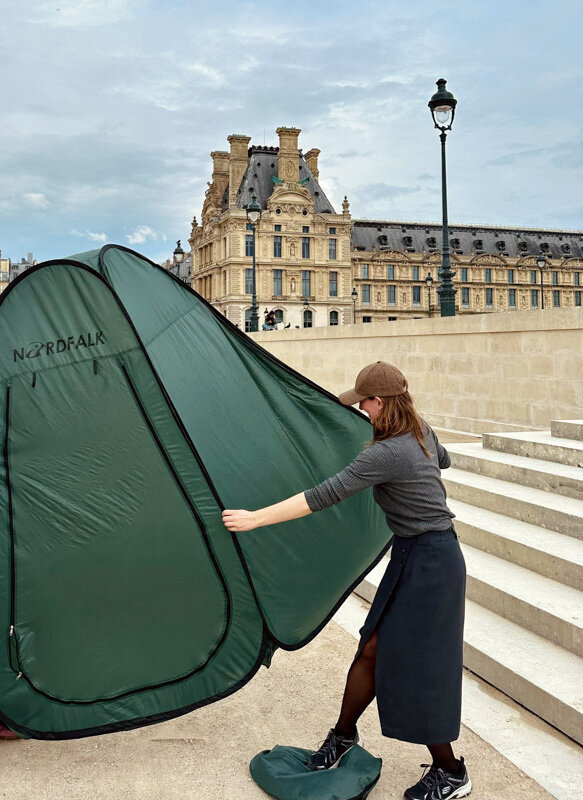 A female photographer is setting up a foldable tent for the model to change clothes in the streets of Paris