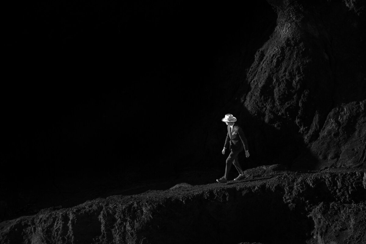 Black and white image of a person walking across rocks