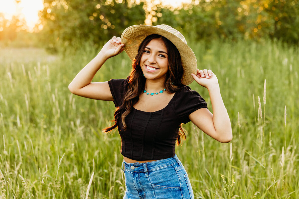 picture perfect teen girl smiling as she holds the sides of her sunhat during her Appleton senior photography session