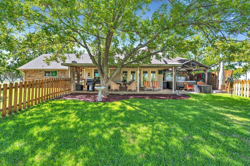 Fenced in backyard and patio with seating and hot tub area at this three-bedroom, two-bathroom vacation rental home with hot tub, firepit, and free WiFi just minutes from Lake Waco.