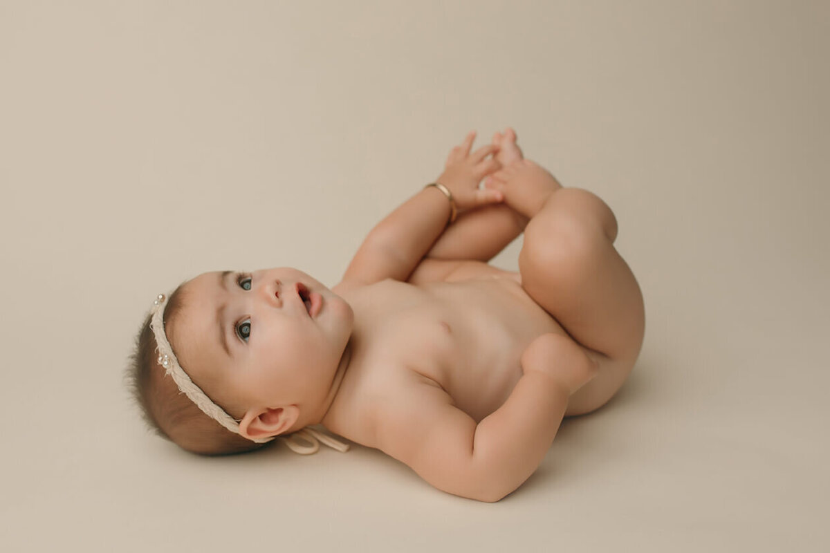a six month old girl laying on her back looking up and grabbing her feet