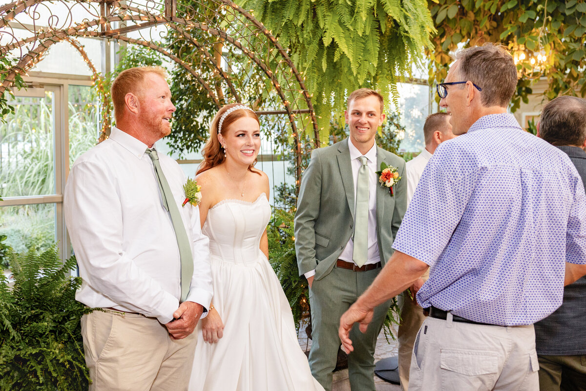 The bride and groom share a warm conversation with family and guests under the lush greenery and twinkling lights at Le Jardin