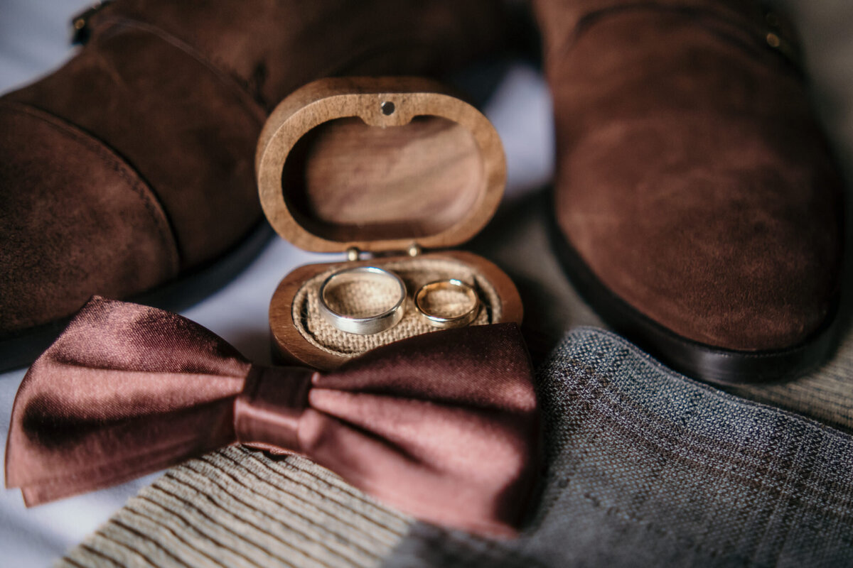 Deatilshot of the wedding rings in a wooden box with the grooms tie.
