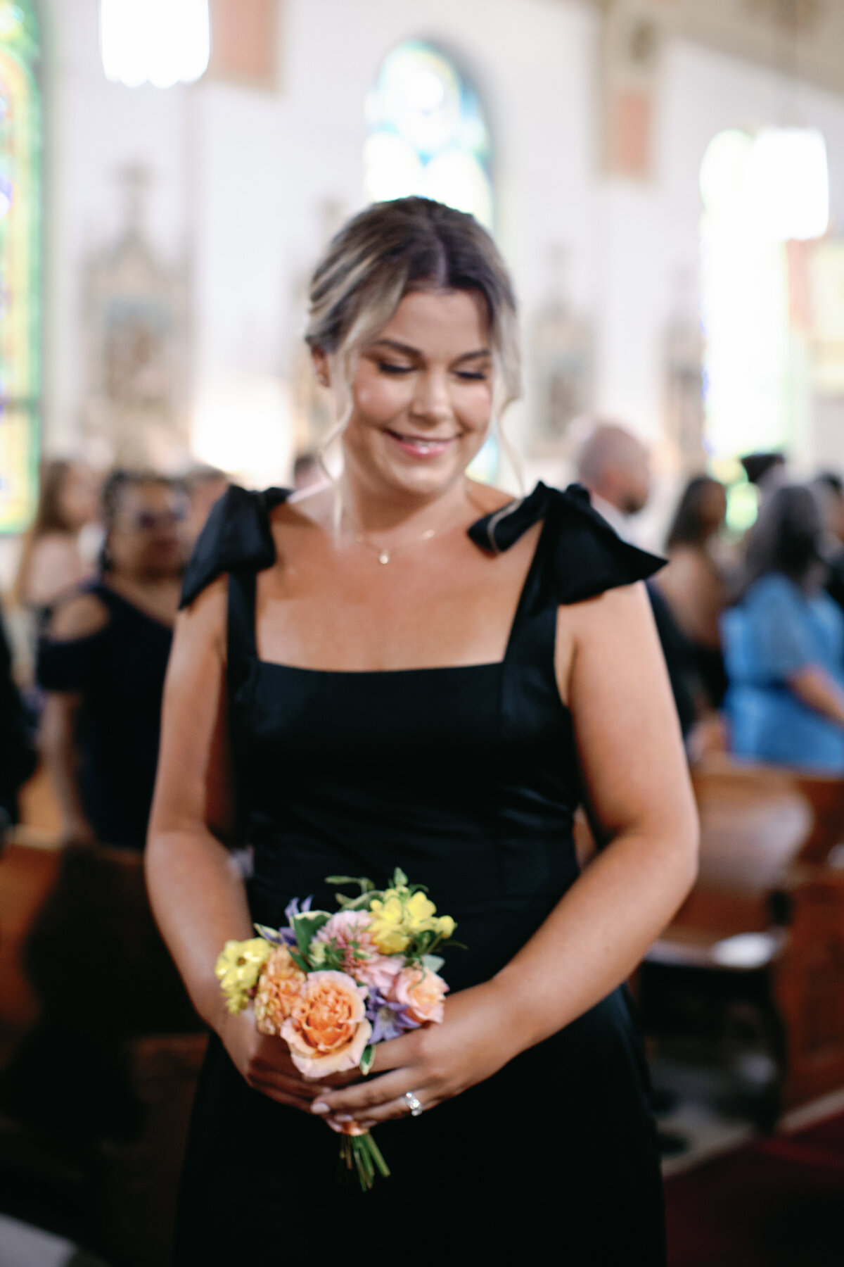 Bridesmaid carrying colorful bouquet of roses and ranunculus designed by Helen Olivia Flowers in Washington DC Catholic church wedding.