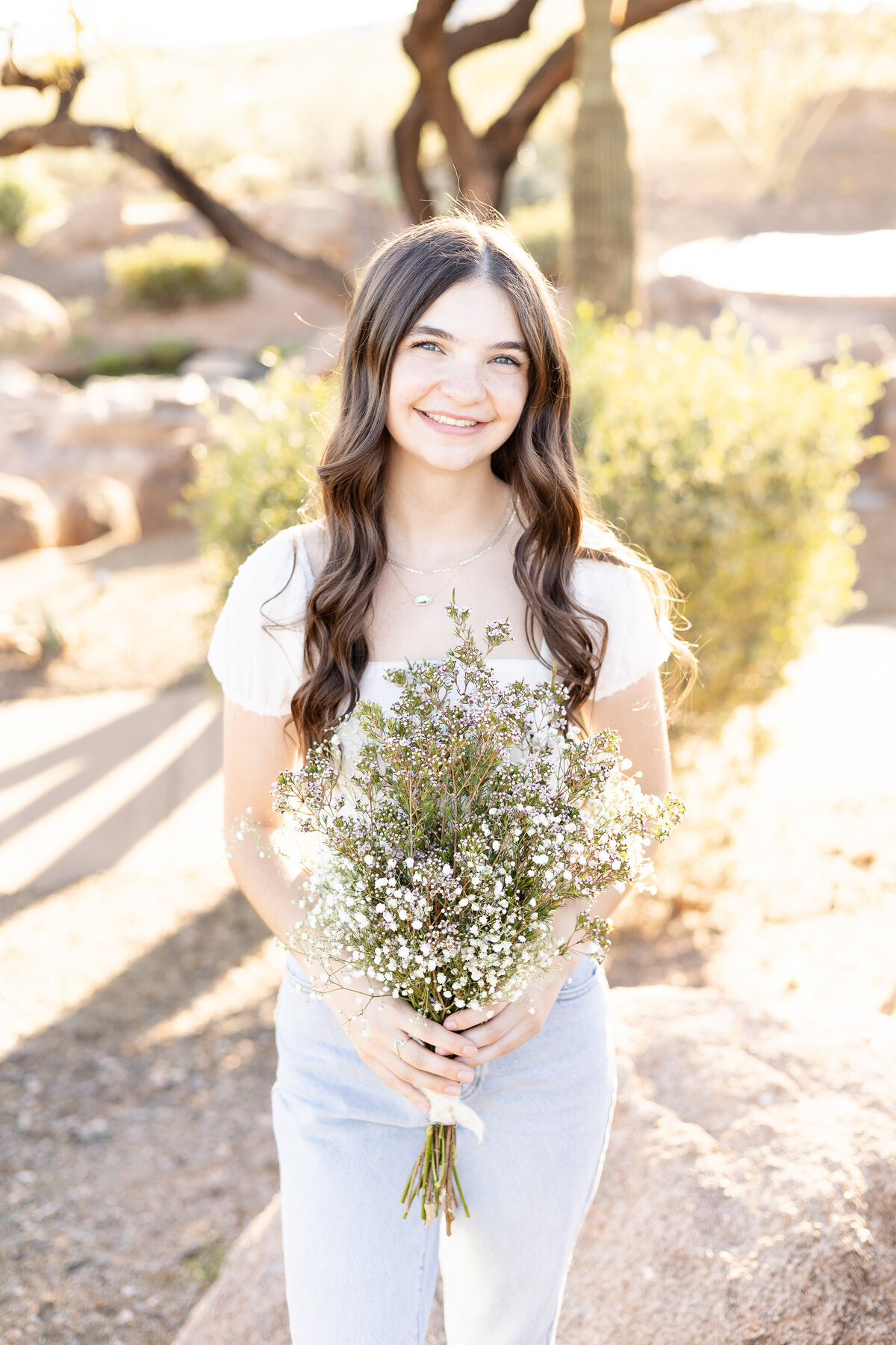 Senior girl smiles while holding floral bouquet in Peoria, Arizona neighborhood of Vistancia.