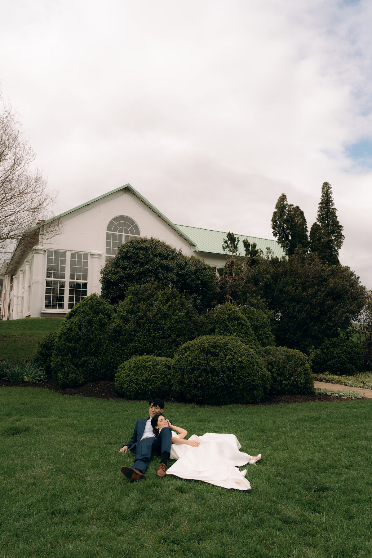 A bride and groom laying in the grass outside of their nashville wedding venue