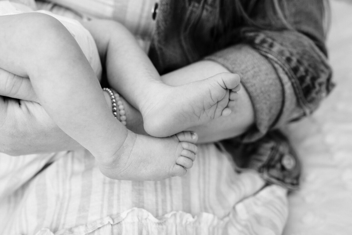 A black-and-white close-up shot of a baby's small feet and legs being gently held by an adult, emphasizing the delicate and tiny features of the baby.