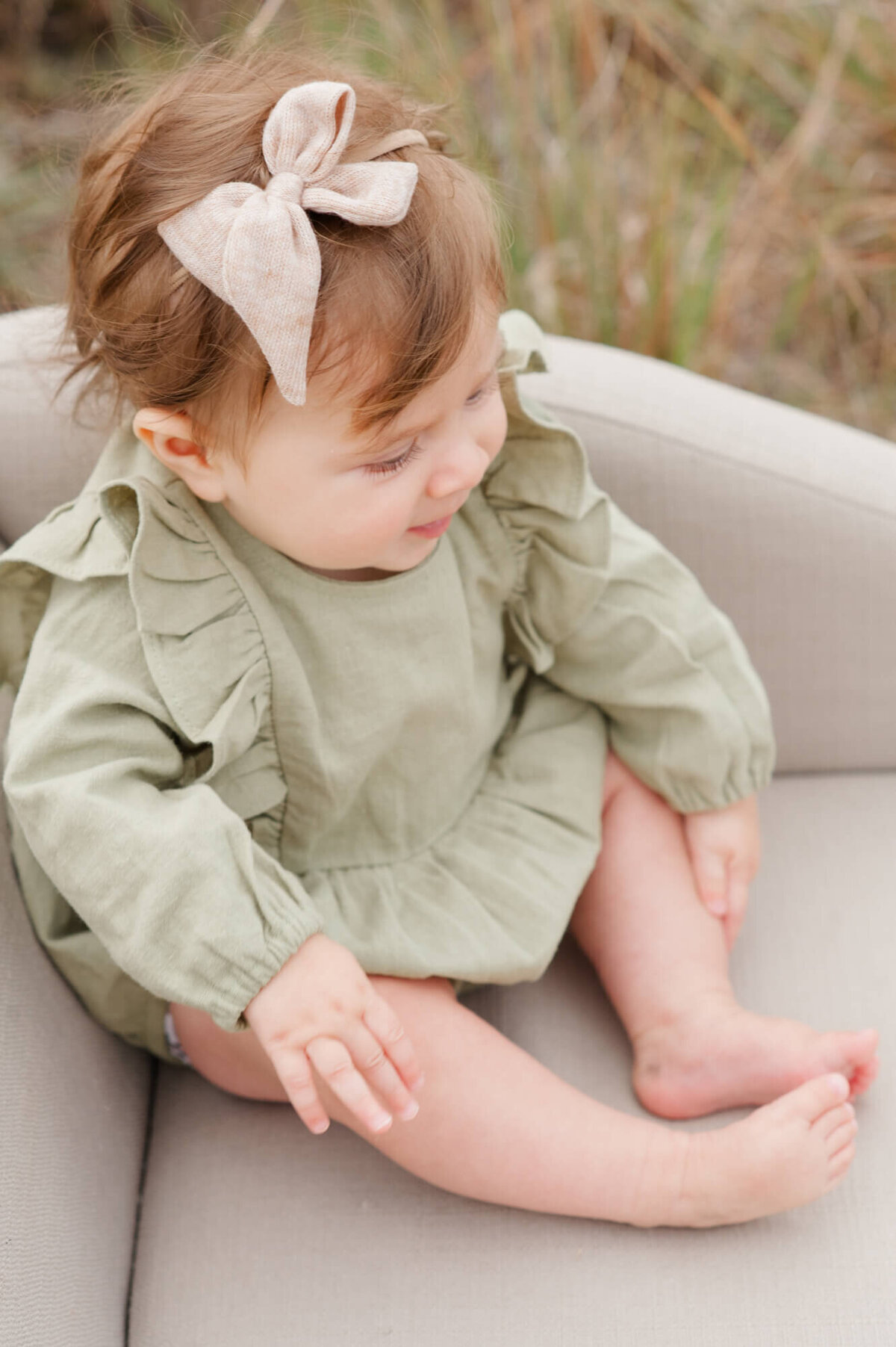 Young girl sitting on a small couch closeup of her bow and green outfit
