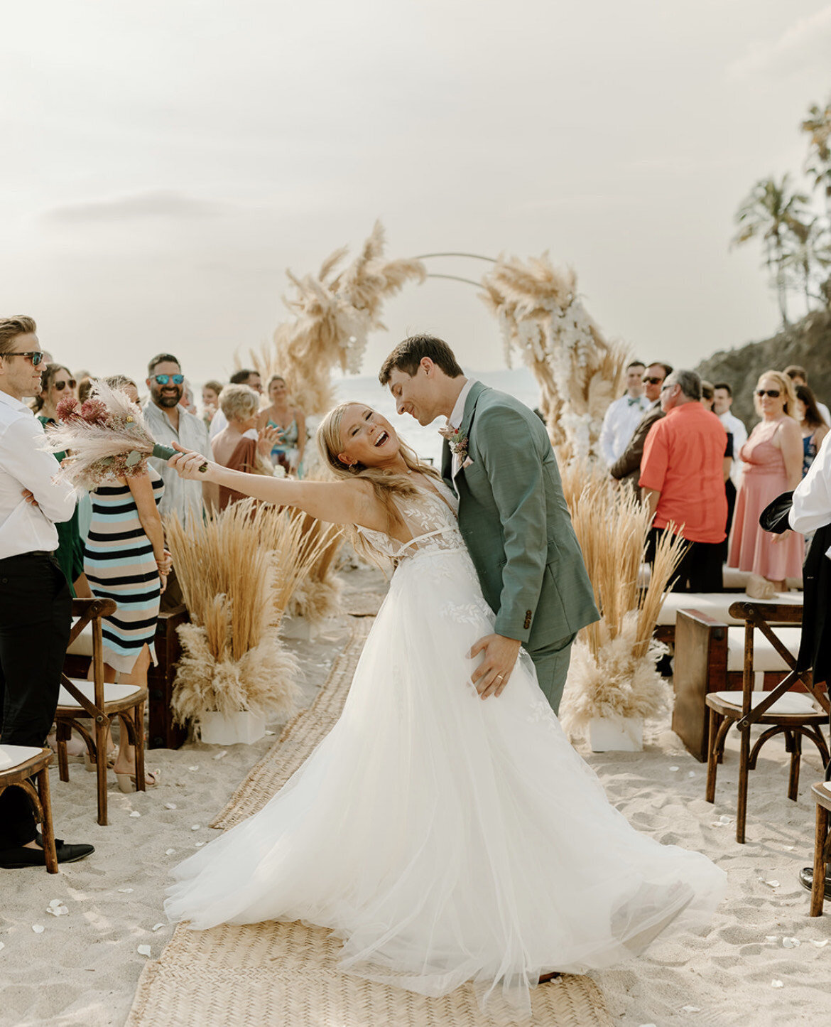 Bride and groom celebrating at a beachfront destination wedding with the bride styled by a Mobile Makeup Artist near me specializing in wedding mobile hair and makeup for tropical ceremonies.