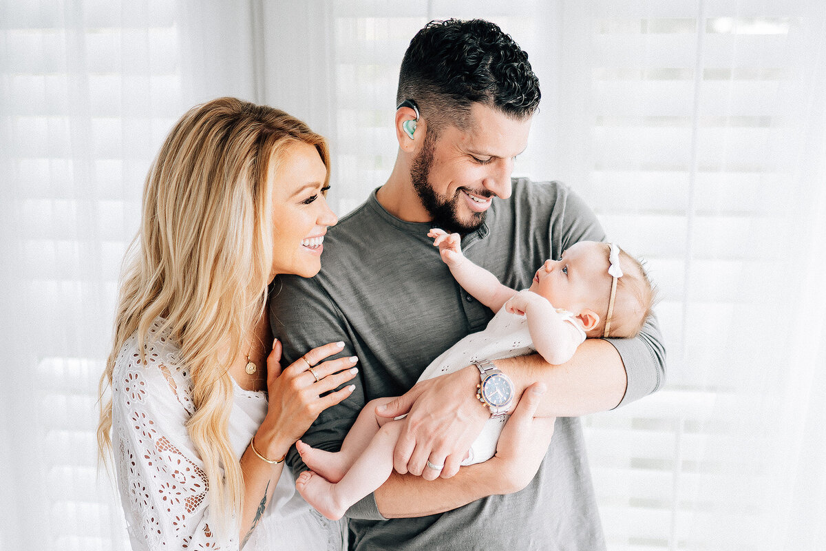 dad who is hard of hearing holding and looking at his newborn baby while mom snuggles his arm