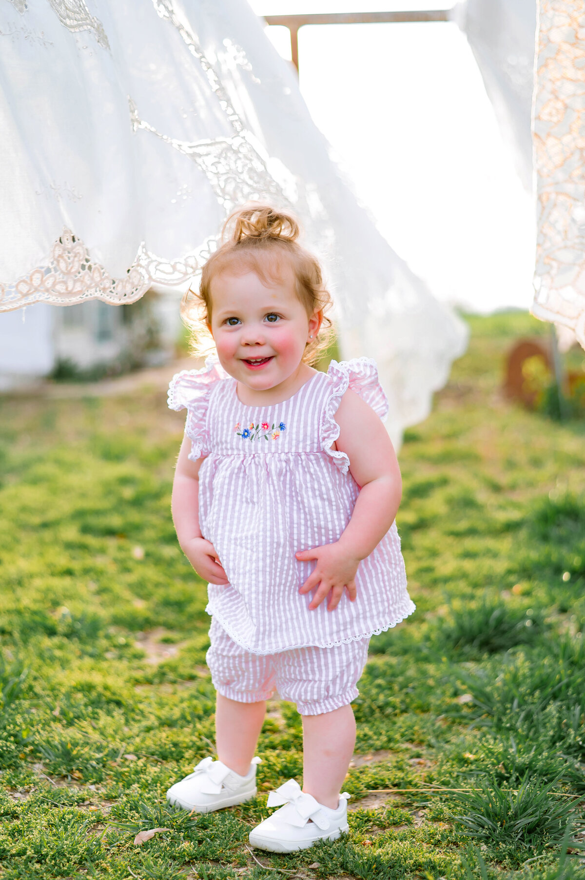 Smiling toddler in a field during sunset photographed by Jennifer L. Kirk Photography in McKinney, Texas. Playful outdoor child portrait with natural light and warm tones.