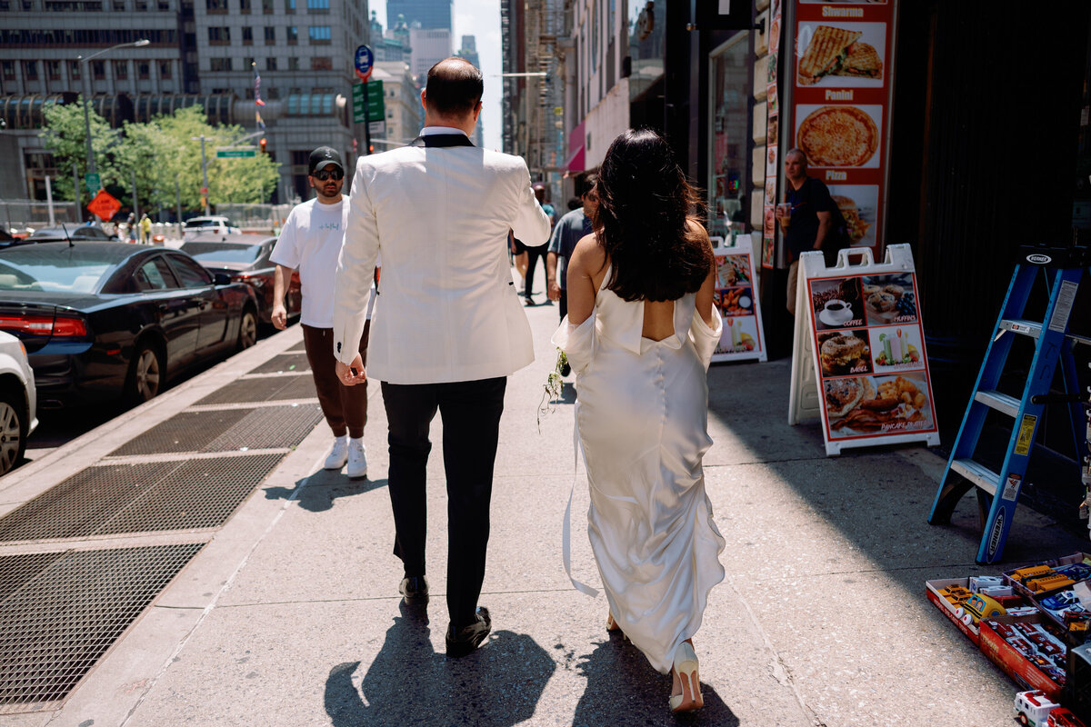 Bride and groom walk hand in hand through the streets of New York City after their City Hall elopement, the bride’s silk gown trailing behind her.