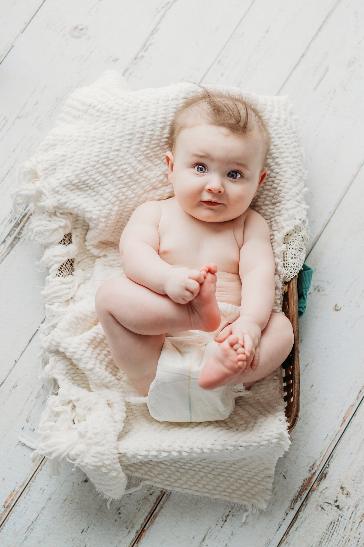 baby boy in a simple white basket holding his feet by harrisburg pa baby photographer
