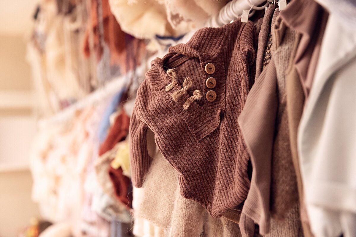 Close-up of hanging newborn photography outfits featuring textured fabrics, soft tones, and detailed buttons.