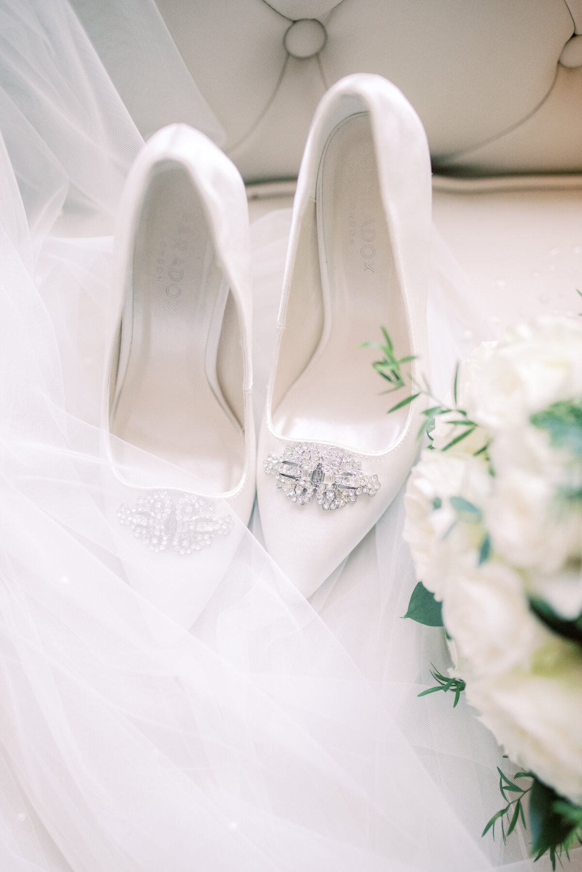 Bridal shoes and bouqet placed with the veil . the image is edited in a light and airy style