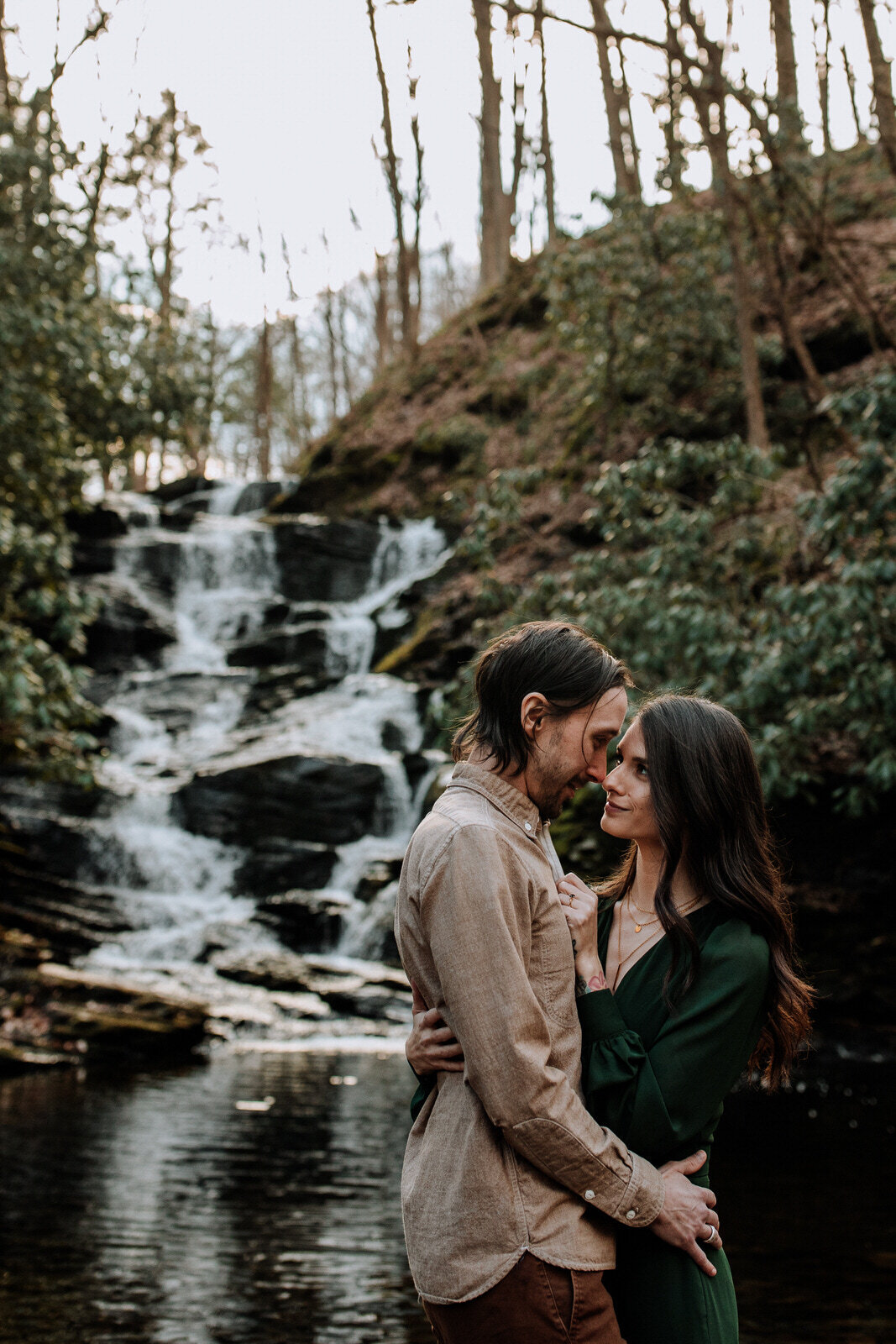 Bride and groom holding hands looking at each other while standing in front of rolling hills with the sunlight coming down on them