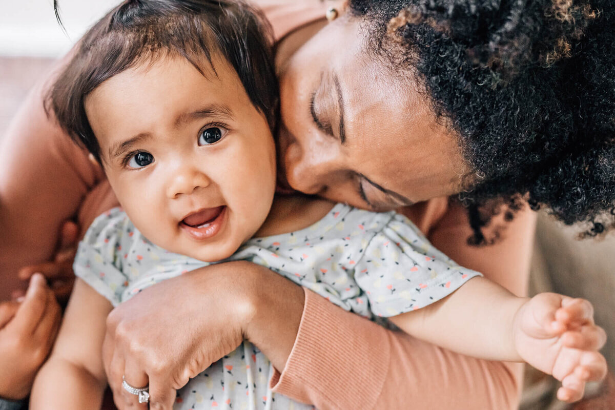 A mom sits with her older baby in her lap, hugging and breathing her in.