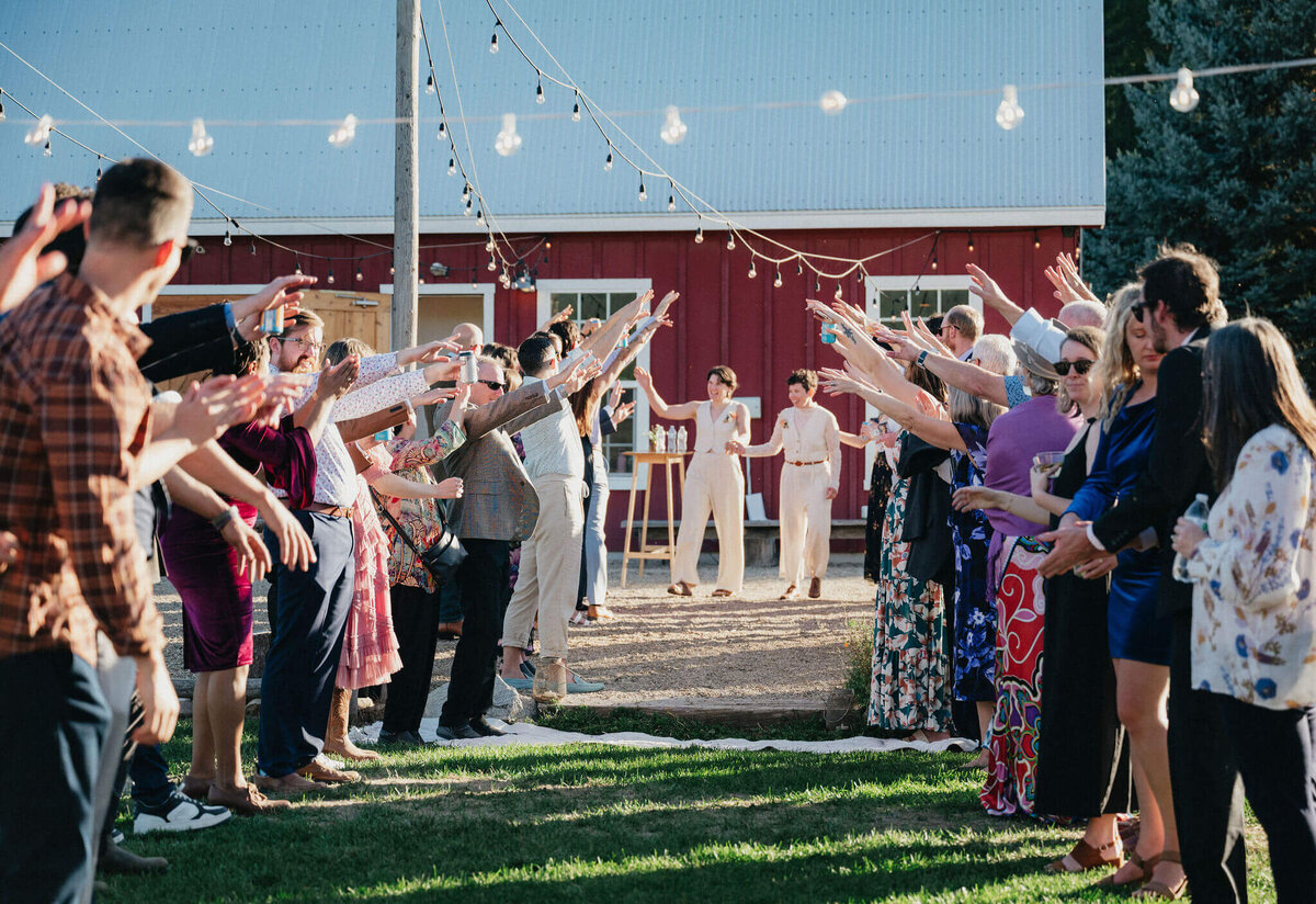 Wedding guests welcoming married couple with raised arms in celebration.