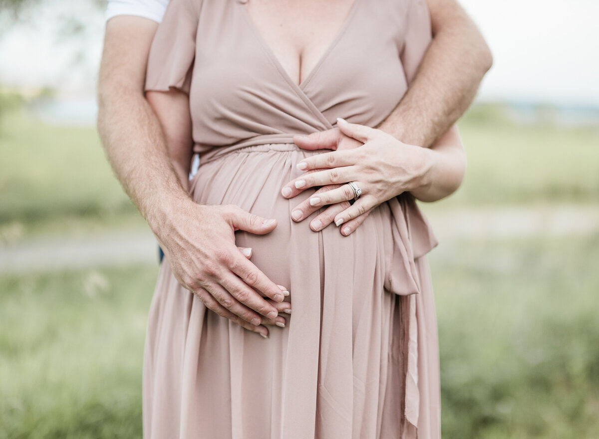 Close-up of expecting couple’s hands gently resting on a mauve maternity gown during an outdoor Kansas City session.