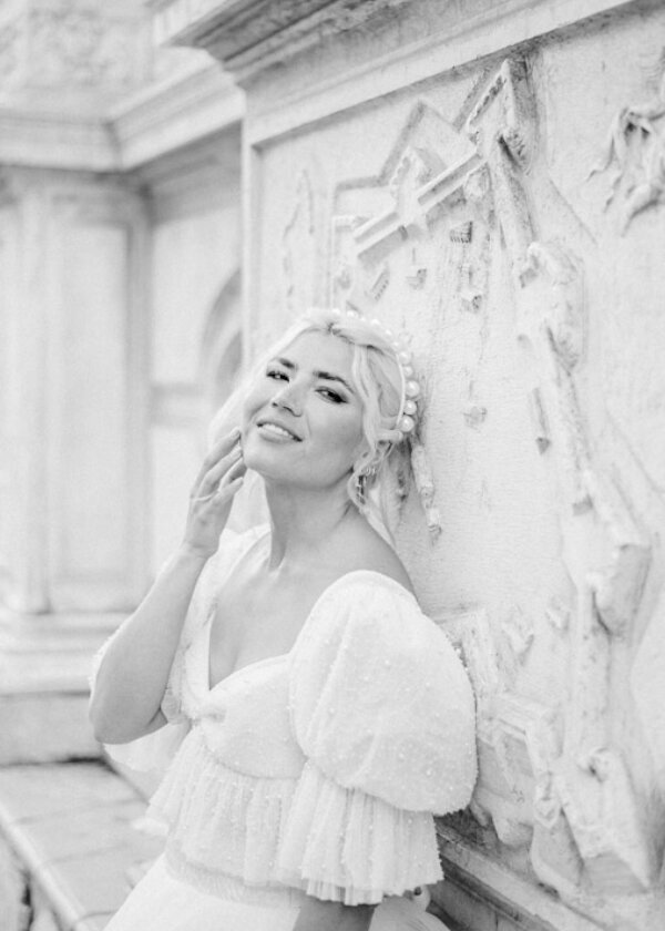 The bride leaning against a marble statue, elegantly posed for their venice engagement session by Christine Grace Photography