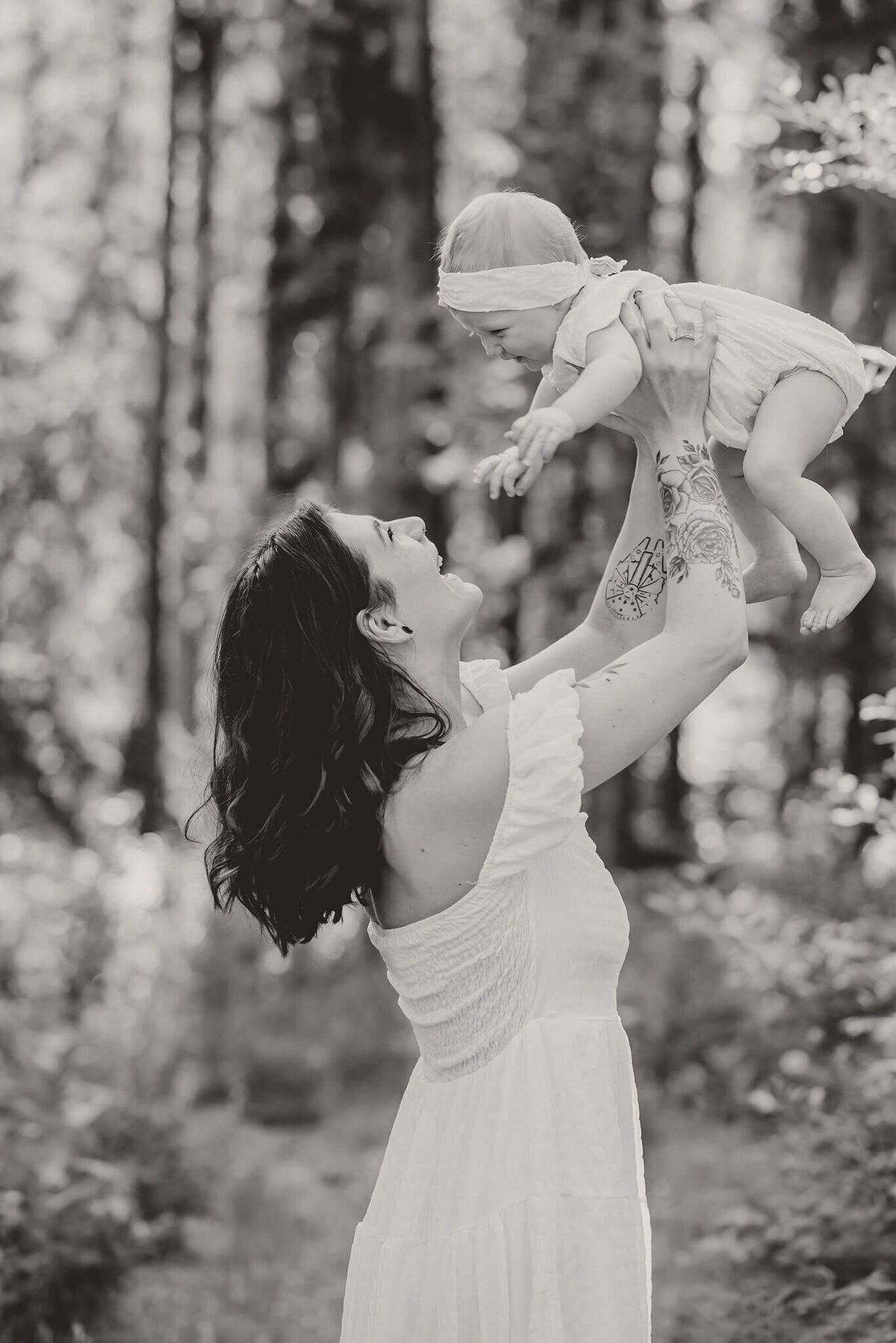 A black and white motherhood portrait. Mother holds her daughter up in the air and they both smile. Portrait by Brittany Danielle in 100 Mile House, BC.