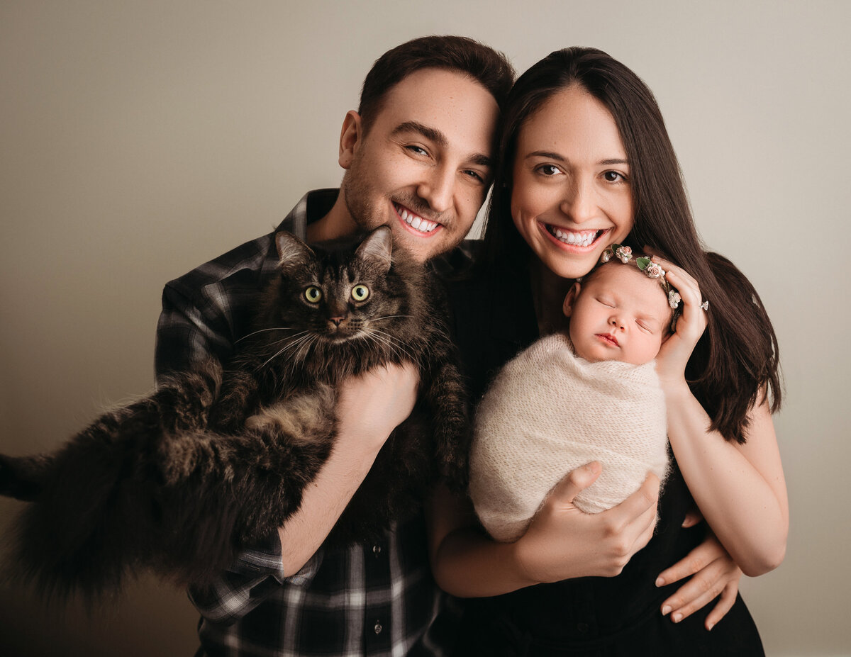 Fairfield County newborn photographer captures  new parents holding their swaddled newborn baby girl and their adorable cat