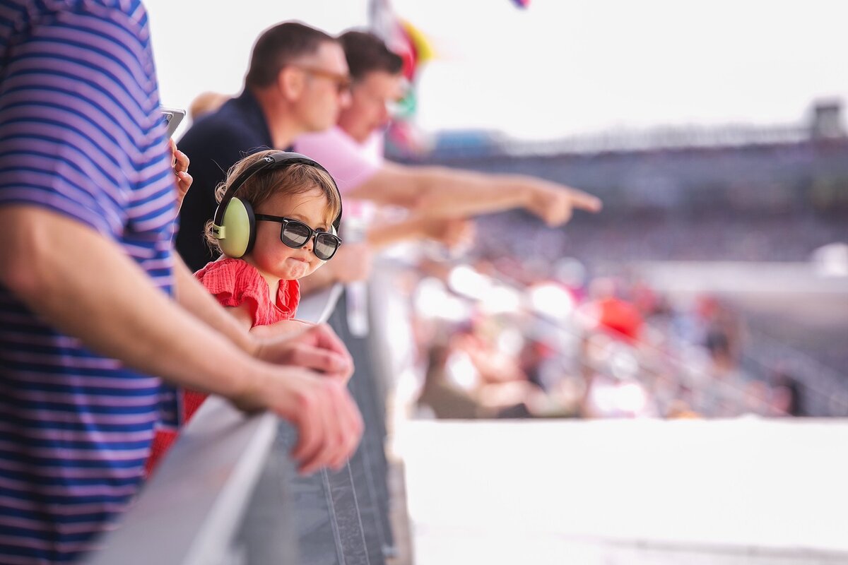 -young-child-wearing-noise-canceling-headphones-and-sunglasses-watches-a-motorsports-event-in-indianapolis-surrounded-by-racing-fans-during-the-month-of-may