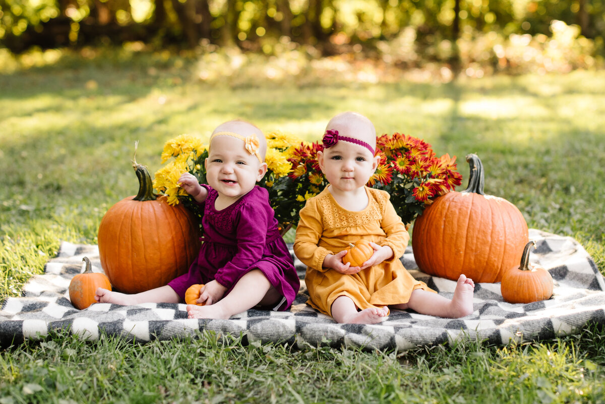 Two babies sitting with pumpkins in fall seasonal colors