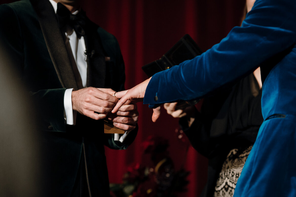 A groom putting on a wedding ring on his groom at their wedding ceremony.