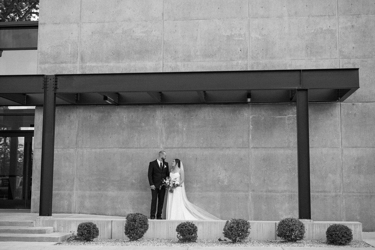 Black and white photo of the bride and groom standing against the iconic brick wall at Leona Road Wedding Venue in Grand Rapids, Michigan. A timeless, editorial wedding portrait.
