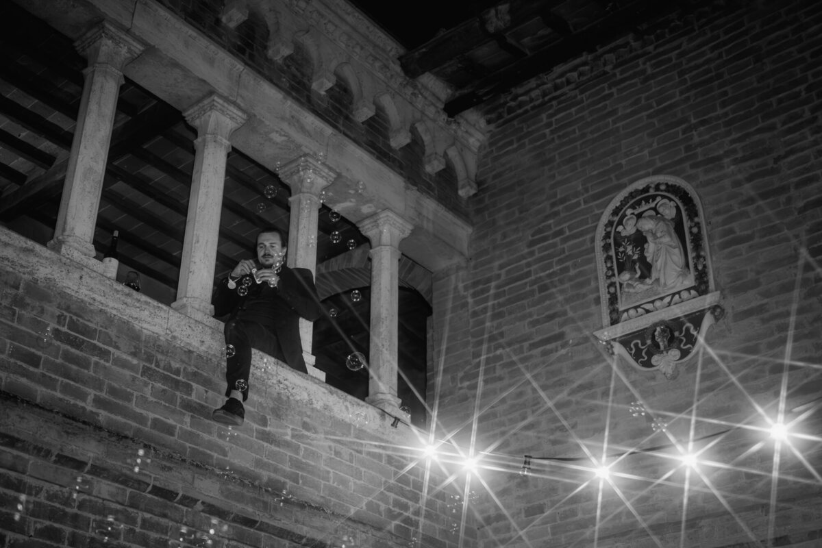 Black and white moment photography where a guest sits on a balkony looking down at the party.