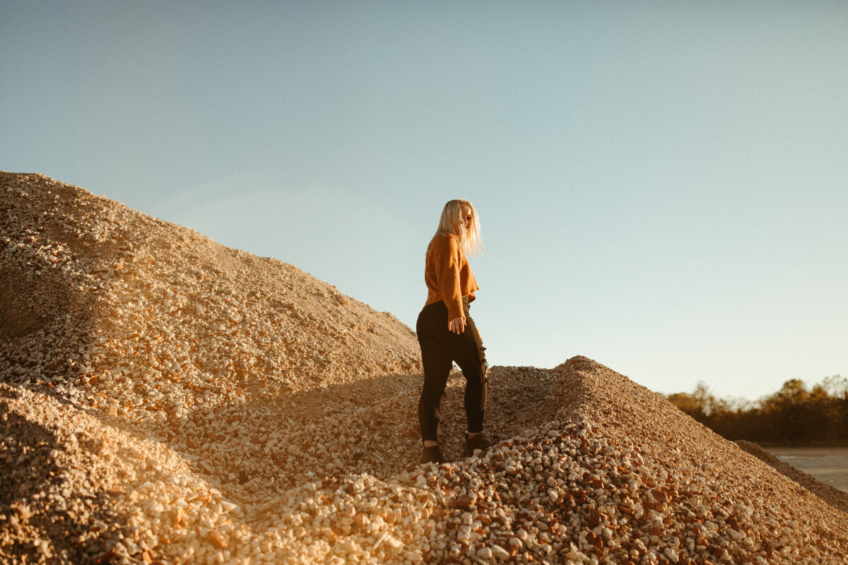 Senior girl in sweater and black pants walking on rock mound