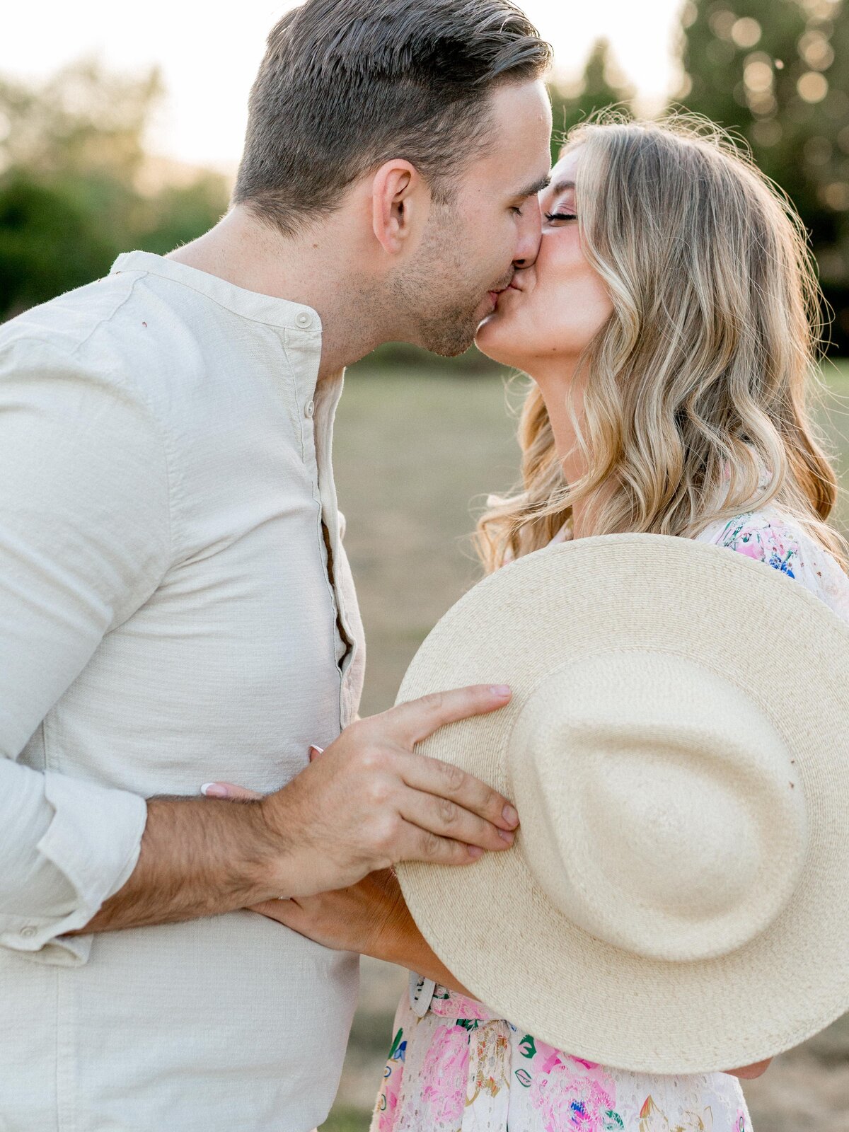 Playful kiss behind a sunhat during a golden hour engagement session in San Luis Obispo—romantic, sweet, and full of charm.