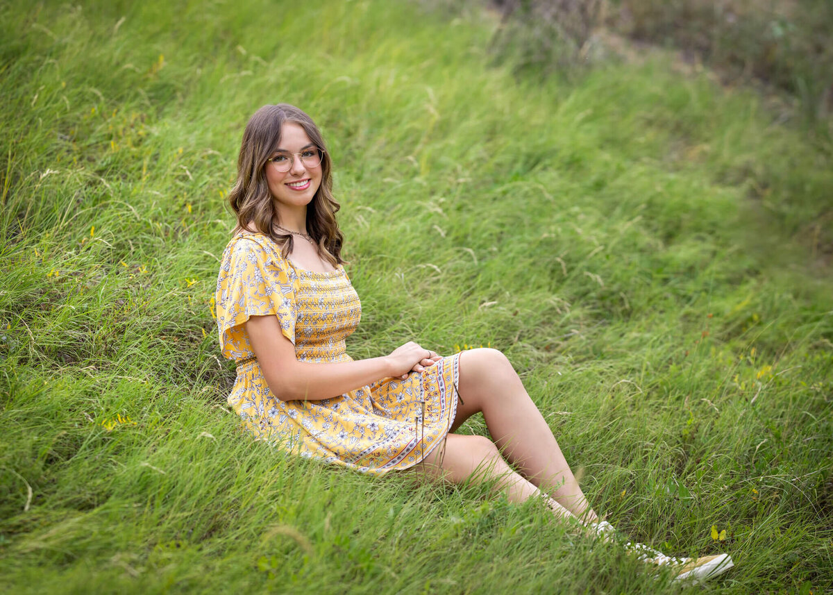 high school senior girl in a yellow sun dress sitting in a grassy field