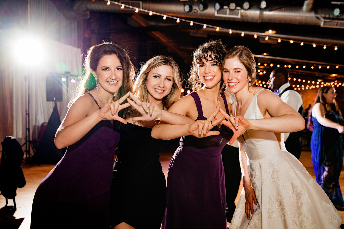 Bride with her sorority sisters on the dancefloor smiling at camera and throwing their hand signs