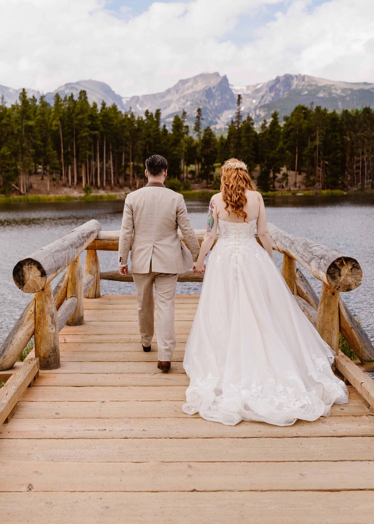 Bride and groom walk across a wooden bridge over Sprague Lake in Rocky Mountain National Park during their wedding day.