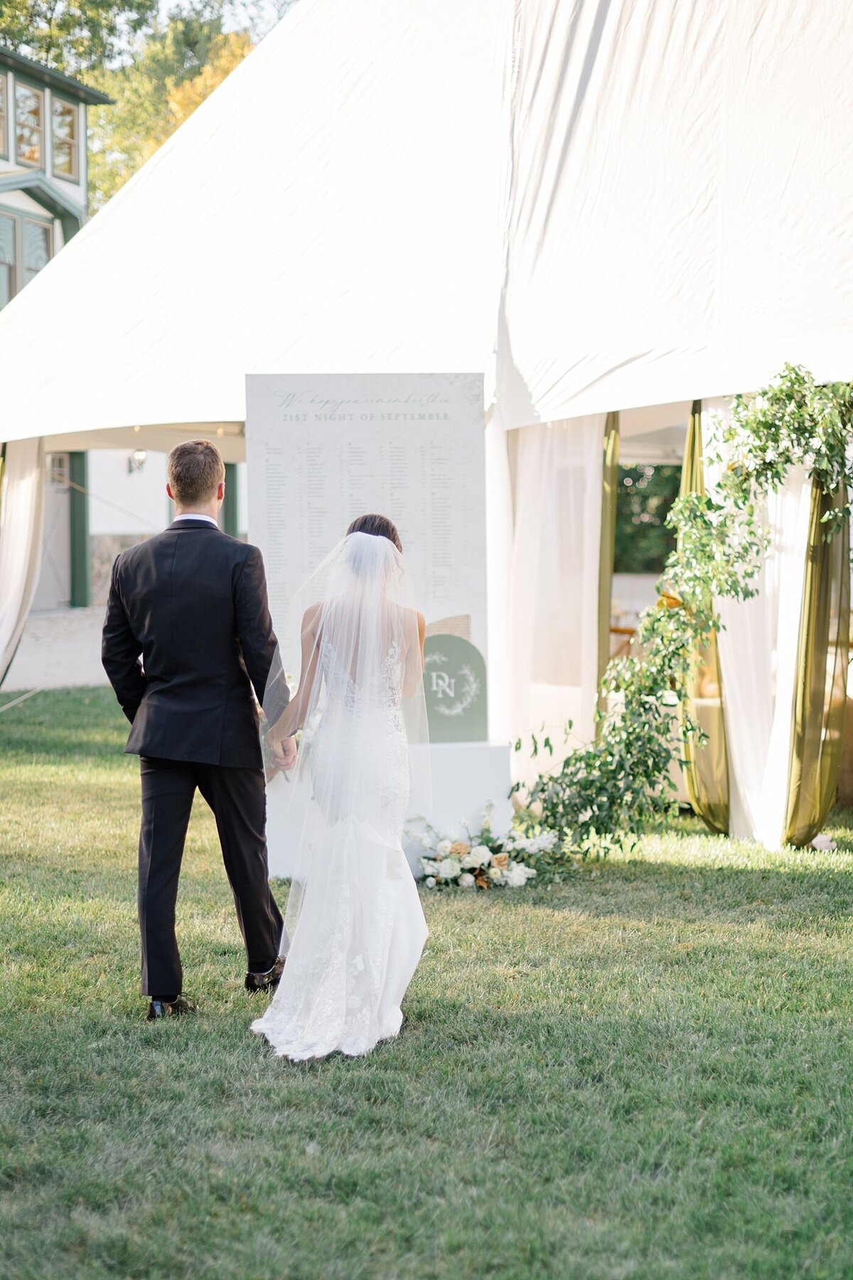 bride and groom holding hands and walking into their white tent backyard wedding reception decorated with lush florals captured by Columbus wedding  photographer