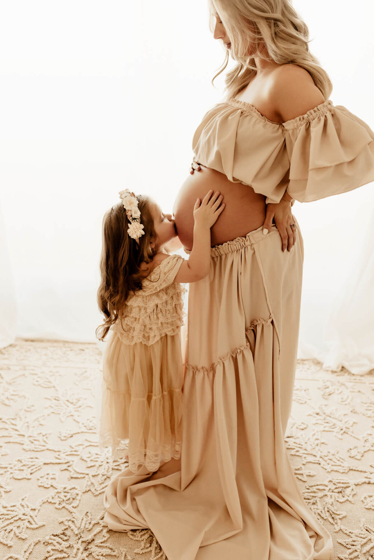 Little girl kisses her mother's belly.