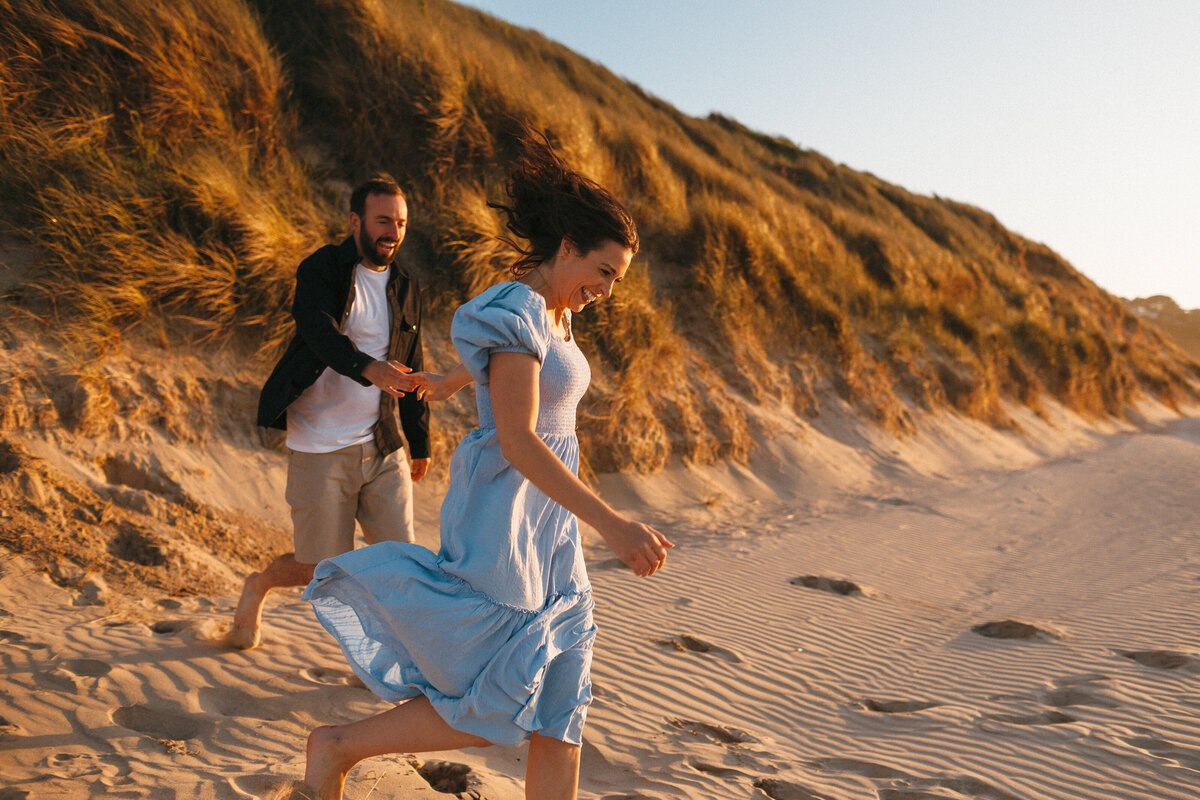 Photograph of a Couple running down sand dunes at sunset in west Cornwall