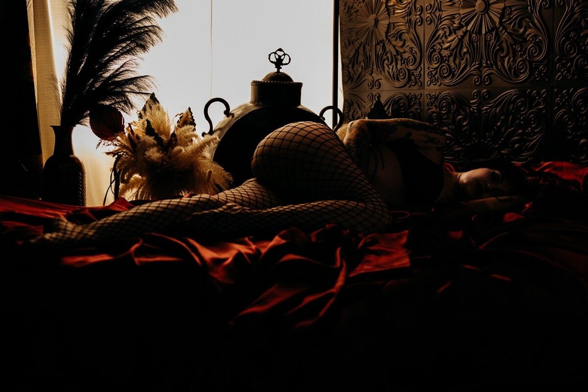 Boudoir photography woman in black fishnets on red sheets in bed Lubbock, Texas Boudoir photographer in Amarillo TX