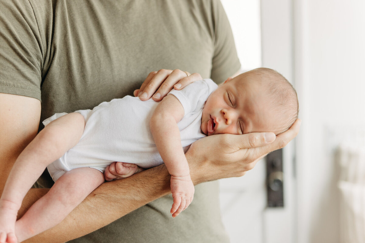 Dad cradles sleeping newborn baby in his palm.